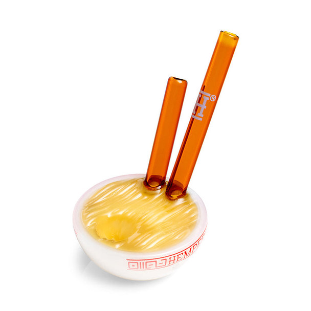 Top angle ramen bowl pipe highlighting textured noodle surface and two amber glass chopsticks, smoke shop restock