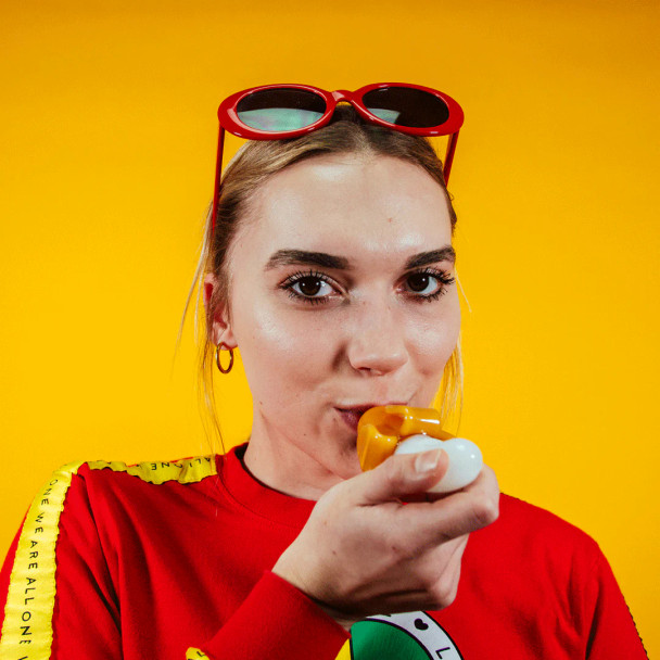 Person holding Goody Glass Bananza hand pipe against yellow backdrop with red sunglasses visible