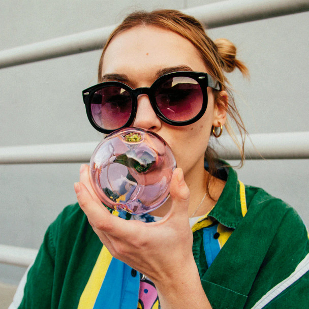 Person holding pink Goody Glass Peachy hand pipe with green stem detail and round glass body