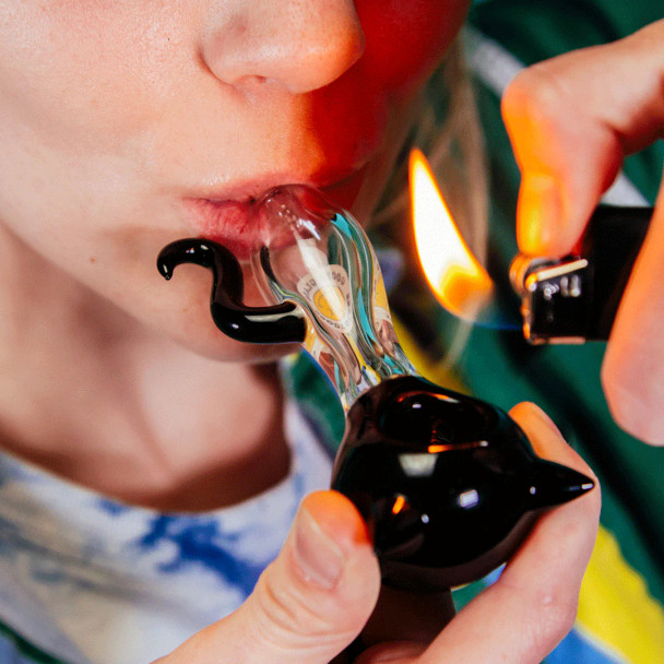 Person using Goody Glass Kitty hand pipe with black cat head, clear body, and lighter flame