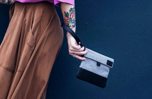 Person carrying a gray and black GRAV smell-proof pouch by the wrist strap to demonstrate compact portable design