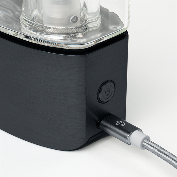 Close-up of black DaVinci EQ base showing side button and braided USB-C charging cable connected