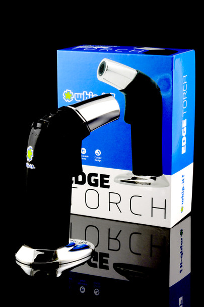 Whip-It Edge torch lighter for wholesale buyers, black with chrome nozzle and tabletop base, left-angle studio shot beside retail box.
