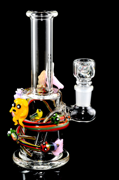 Clear 7" mini beaker rig with rainbow coil accents and character figures, 14.5 mm female joint, glossy black studio—wholesale head-shop concentrate piece.