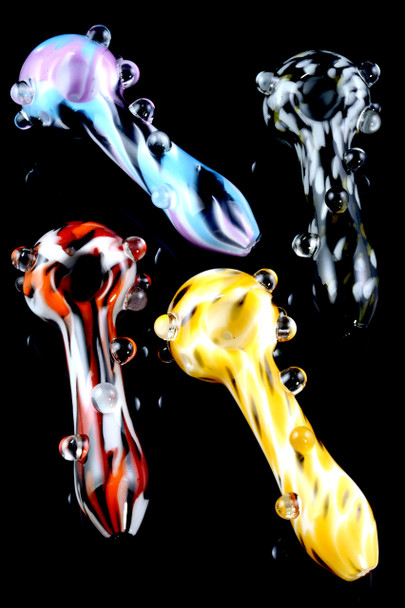 Four 4" psychedelic glass spoon pipes on glossy black, assorted yellow, red, purple/blue, and black/white patterns—head-shop wholesale group shot with marble grips.