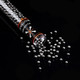 Wholesale carbon bead refill tube pouring activated charcoal pellets against black backdrop, close-up