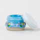 Wholesale donut terp jar, 1.5-inch blue glaze with pastel sprinkle glass, white metal lid tilted beside jar, side angle hero shot on clean backdrop.