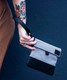 Close-up of gray and black GRAV smell-proof pouch held by removable wrist strap with fold-over flap visible