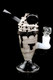 Black-background studio shot of 7" US-made sundae mini rig with cookie topper, chocolate drizzle, clear base; wholesale head-shop rig, right-side angle.