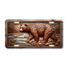 Grizzly Bear license plate featuring rustic mountain stream scene with rocky terrain, pine forest, and bronze tones in embossed-look artwork on aluminum.