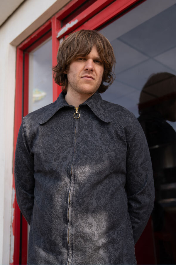 Man wears Madcap England Black/Grey Paisley Print Dagger Collar Shirt Jacket in Denim