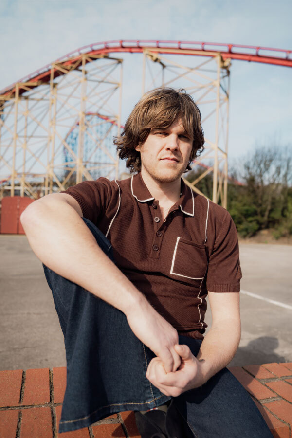 Man wears Madcap England Knitted Piped Mod Polo Shirt in brown