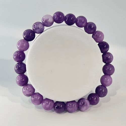 A centered, top-down view of a single lepidolite beaded gemstone stretch bracelet wrapped around a circular white display stand. The uniformly sized, round crystal beads feature a smooth, glossy finish with natural shades ranging from light pastel lilac to deep violet and magenta-purple.