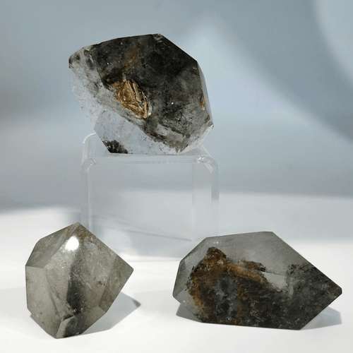 Three chunks of natural Garden Quartz in free form shapes. The clear crystal contains distinct dark, mossy brown and black mineral inclusions. Three chunks of natural Garden Quartz in free form shapes. The clear crystal contains distinct dark, mossy brown and black mineral inclusions.