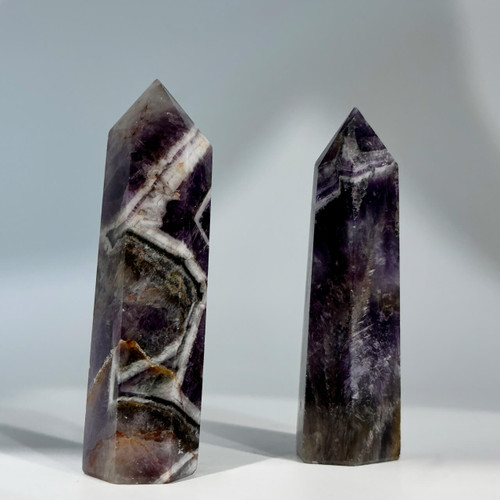 A photo of two polished amethyst crystals, one with distinct white and purple chevron patterns and the other with swirled purple hues.