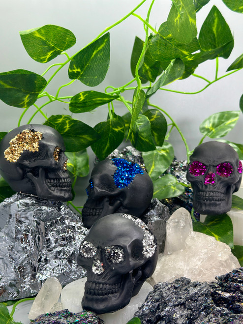 Collection of mini skull with geode figurines showcasing blue, gold, pink, and silver crystal-lined interiors on black decorative skulls.