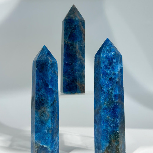 Three vertically-oriented carved crystal towers of blue apatite, showing the mineral's characteristic deep blue color, with visible striations and dark inclusions. Three vertically-oriented carved crystal towers of blue apatite, showing the mineral's characteristic deep blue color, with visible striations and dark inclusions.