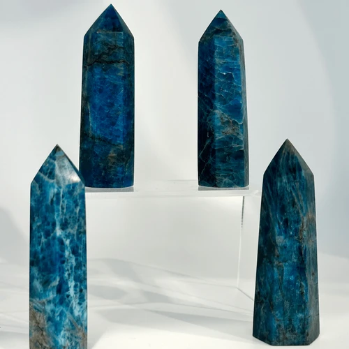 Four blue apatite crystal towers, showing natural striations and a hexagonal shape, stand on a white surface.