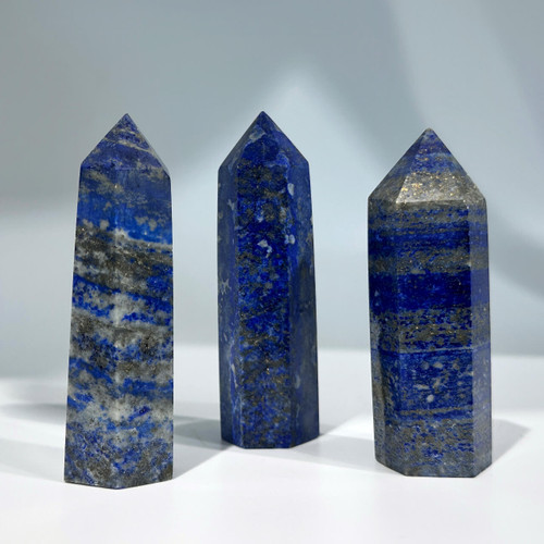 Three polished lapis lazuli crystal points featuring a deep blue base color with marbled patterns of lighter blue, gray, and sparkling flecks of gold pyrite Three polished lapis lazuli crystal points featuring a deep blue base color with marbled patterns of lighter blue, gray, and sparkling flecks of gold pyrite