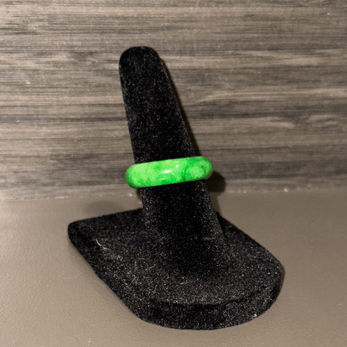 A smooth, polished jade ring with a vibrant, light green color is displayed on a black, felt ring stand. A smooth, polished jade ring with a vibrant, light green color is displayed on a black, felt ring stand.
