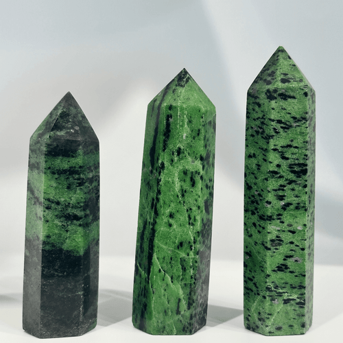 Three polished crystal towers, or points, made of Ruby Zoisite. The hexagonal towers are primarily bright green with heavy black flecks, characteristic of the mineral Zoisite. The crystals stand upright against a white background, varying slightly in height and width.