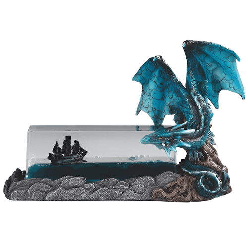 A decorative fantasy statue featuring a vibrant teal and blue dragon with translucent wings perched on a rocky base. To the left of the dragon is a rectangular clear acrylic block containing blue liquid and a small black pirate ship that appears to float. The dragon is leaned over, looking intently at the ship inside the bottle.