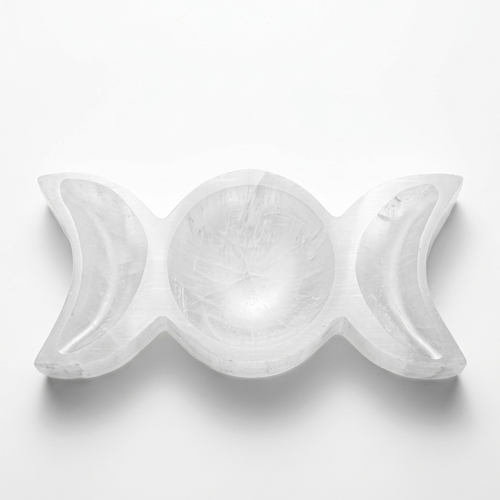 A hand-carved Triple Moon goddess bowl made from translucent white selenite, featuring a central circular basin flanked by two crescent moons.