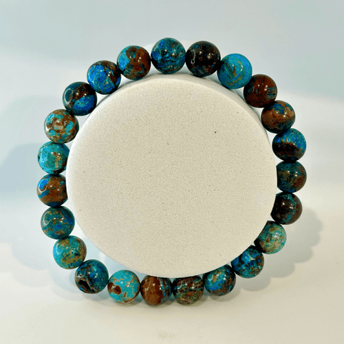 A centered, top-down view of a single natural blue kyanite beaded stretch bracelet. The round, highly polished gemstone beads exhibit a stunning variety of deep sapphire blue and silvery-blue hues, displaying the characteristic fiber-like, shimmering chatoyancy of kyanite against a clean white background.