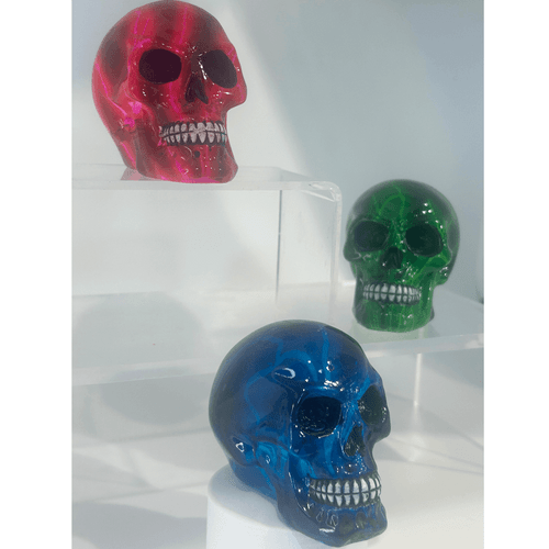 Miniature decorative skulls with a high-gloss, opaque finish in vibrant pink, green, and blue, featuring striking electric lightning vein patterns and detailed teeth.