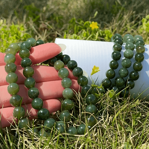 Natural Jade gemstone bead bracelet displayed outdoors in natural light resting near greenery and yellow wildflowers.