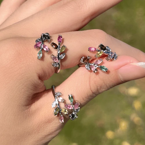 Close-up of a hand wearing multicolored gemstone vine rings with leafy branches and adjustable bands.