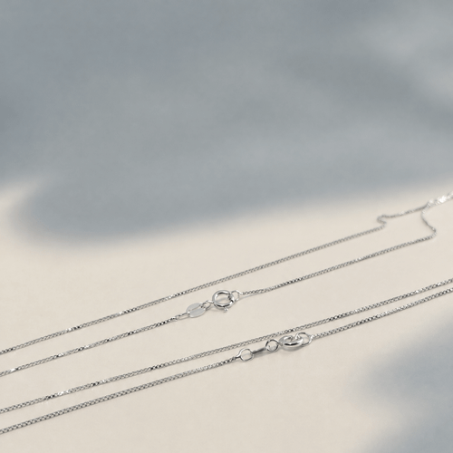 Thin sterling silver chain necklace laid flat, showcasing its delicate design and polished silver finish against a neutral background.