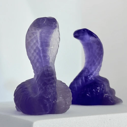Indigo fluorite cobra carving featuring two raised serpent heads in deep purple and violet tones on a light background.