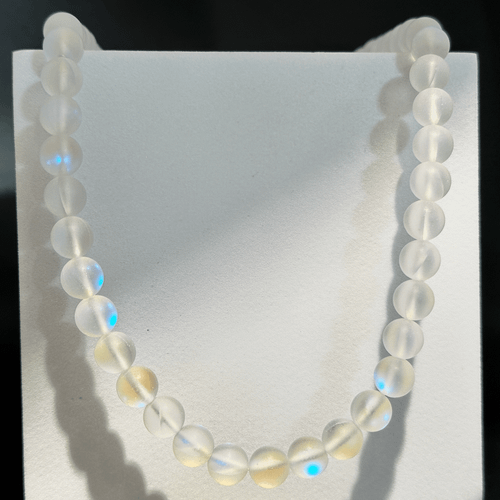 Aura Necklace featuring iridescent round beads with soft pastel blue, yellow, and rainbow reflections, displayed hanging against a light background.