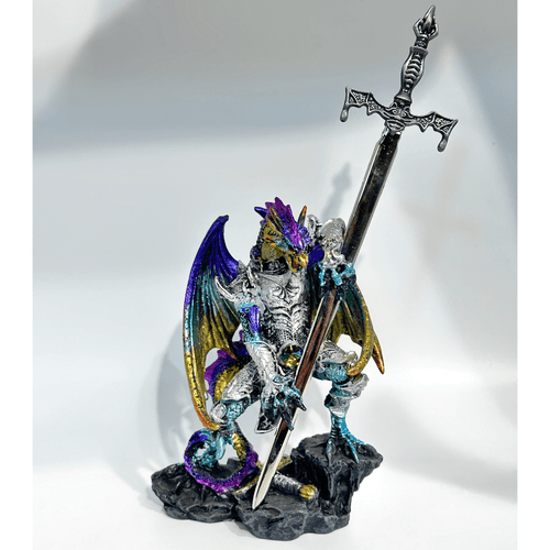A decorative letter opener featuring a metallic rainbow-armored dragon warrior. The dragon has iridescent purple, gold, and blue scales and stands on a grey rocky base while holding a large, silver-toned knight's sword. The sword is removable and serves as a functional letter opener with a detailed bat-wing hilt.