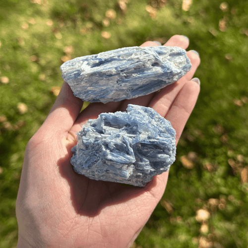 Rough blue kyanite mineral specimens with silvery-blue layered textures resting on a person's palm outdoors.
