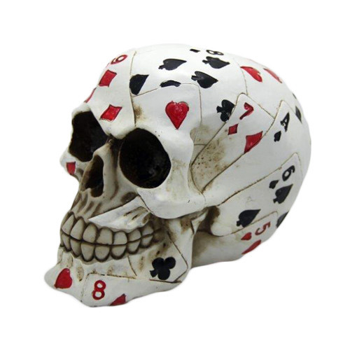 Left profile view of a white cold-cast resin Poker Skull statue decorated with red and black playing card suits.
