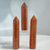The crystals are reddish-orange to warm peach in color, with a visible shimmer or aventurescence characteristic of sunstone. They are carved into tall, six-sided obelisk shapes with sharp points.