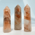 A trio of hexagonal Red Fire Quartz wands, each featuring a clear body with dramatic, fiery reddish-brown and orange mineral inclusions throughout. A trio of hexagonal Red Fire Quartz wands, each featuring a clear body with dramatic, fiery reddish-brown and orange mineral inclusions throughout.