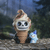 Ice cream resin figurine of a skull cone next to a small blue penguin, positioned on a rustic surface with a blurred forest in the background.