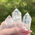 A hand holds three polished, clear quartz crystal tower points against a blurred background of green grass and sunlight. A hand holds three polished, clear quartz crystal tower points against a blurred background of green grass and sunlight.