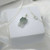 Close-up of a Hello Kitty jade pendant with a silver chain resting on a white jewelry gift box, showcasing natural green jade.