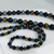 Close-up of Triple Protection necklaces in 6mm and 12mm bead sizes. The shot highlights the natural textures and high-luster finish of the Obsidian, Tiger Eye, and Hematite stones, emphasizing the quality of the hand-selected beads.
