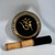 A dark bronze singing bowl with ornate gold patterns on its exterior, featuring a prominent gold Om symbol on its bottom. A felt-tipped mallet rests nearby.