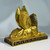 A golden, winged Egyptian sphinx statue, viewed from the back, showing its striped headdress and prominent wings, on a decorative black base.