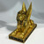 A golden, winged Egyptian sphinx statue, depicting a pharaoh's head and lion's body, on a black and gold decorative base.