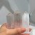 A hand holds three semi-translucent selenite crystal towers. The towers have a striated, fibrous texture and pointed tops.