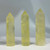 Three polished citrine crystal towers, each with a pointed top, show varying levels of clarity and a pale yellow hue. Natural striations and inclusions are visible within the crystals.