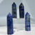 A polished lapis lazuli crystal point stands upright, featuring a deep blue color with marbled light blue and gray patterns and flecks of gold pyrite.