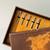 A close-up, angled shot of a brown, patterned gift box. Inside, five metallic pen nibs are neatly arranged in a row, resting on a yellow, textured lining. A close-up, angled shot of a brown, patterned gift box. Inside, five metallic pen nibs are neatly arranged in a row, resting on a yellow, textured lining.